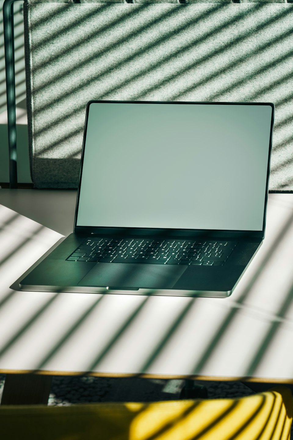 An open laptop rests on a desk with striped shadows.