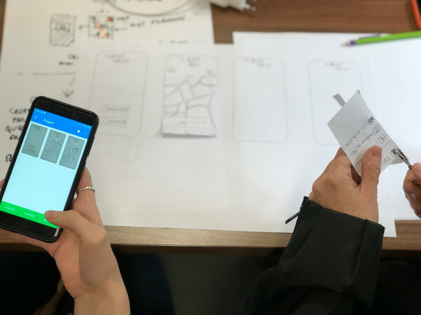 Hands working on app design with sketches and smartphone.
