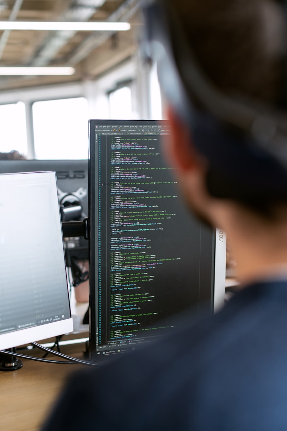 Programmer focused on code on two computer monitors.